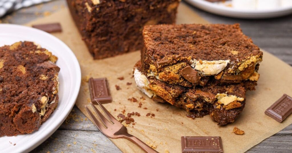 A horizontal image featuring sourdough s'mores banana bread that has been sliced and displayed on a piece of parchment paper.