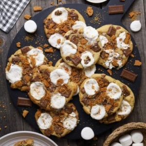 Recipe feature image for S'mores Sourdough Cookies. There are 7 cookies photographed from above. They are sitting on a round, black serving platter.