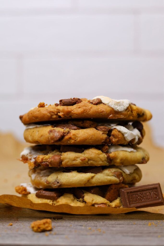 A stack of 5 sourdough s'mores cookies photographed close up. You can also see a piece of Hershey's Milk chocolate sitting in front of the stack.
