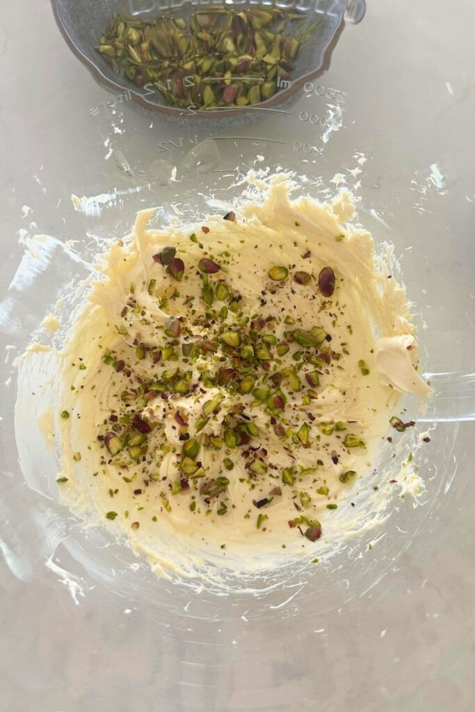 Honey pistachio cream cheese being made with pistachios added to cream cheese in glass bowl.