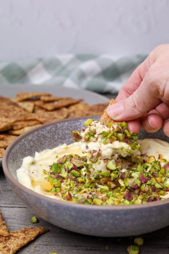 Honey pistachio cream cheese in a serving bowl with a hand dipping a cinnamon sugar cracker.