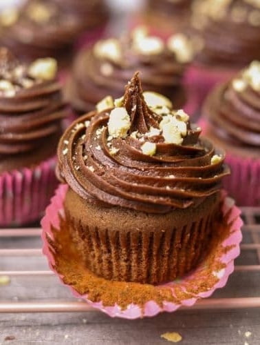 A close up photo of a sourdough chocolate cupcake topped with chocolate frosting and sprinkled with toasted hazelnuts.
