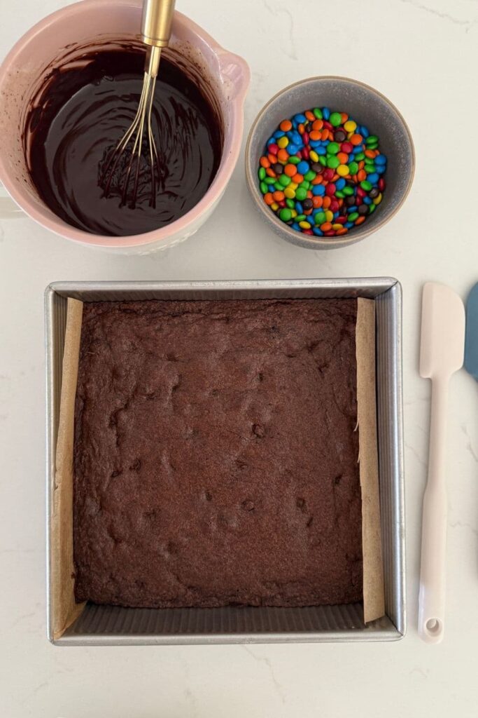 Sourdough cosmic brownies baked in pan next to ganache and candy topping.