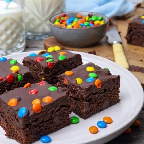 Sourdough cosmic brownies sliced on a white plate with a bowl of m and m candies in background.