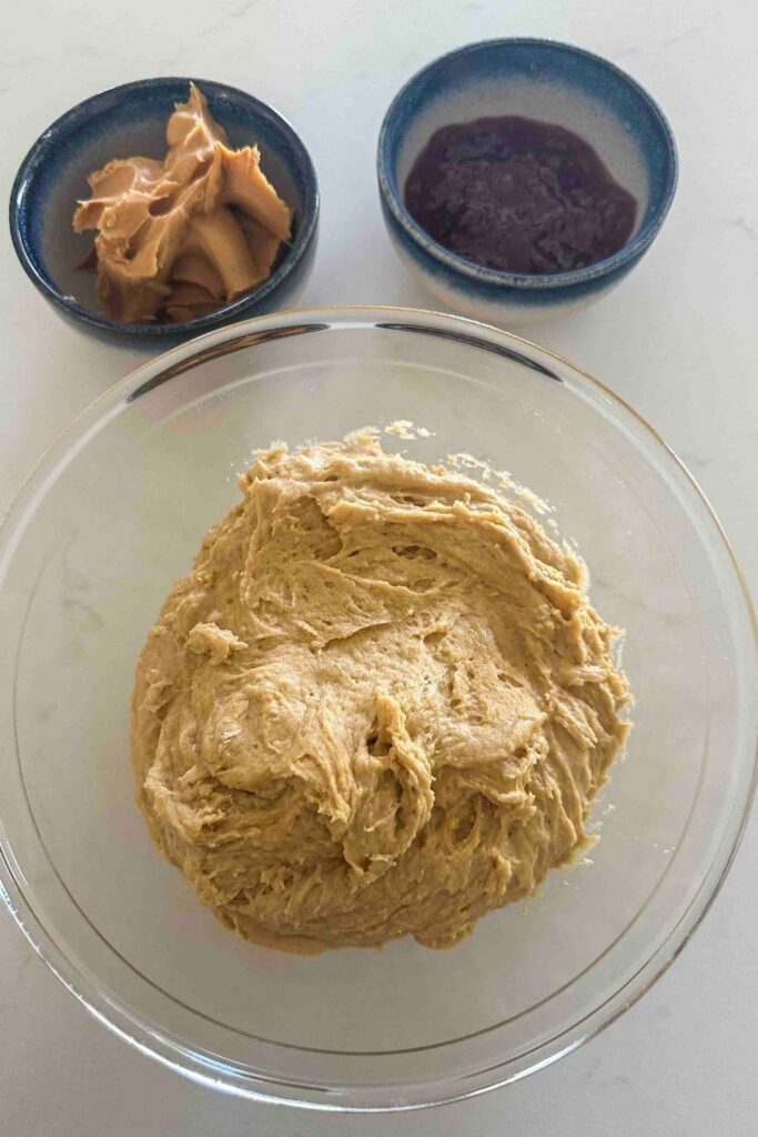 glass bowl of sourdough peanut butter and jelly cookie dough next to a bowl of peanut butter and a bowl of jelly.