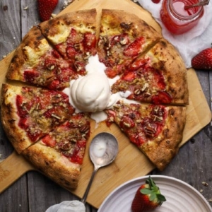 A sourdough strawberry crumble pizza topped with vanilla ice cream.