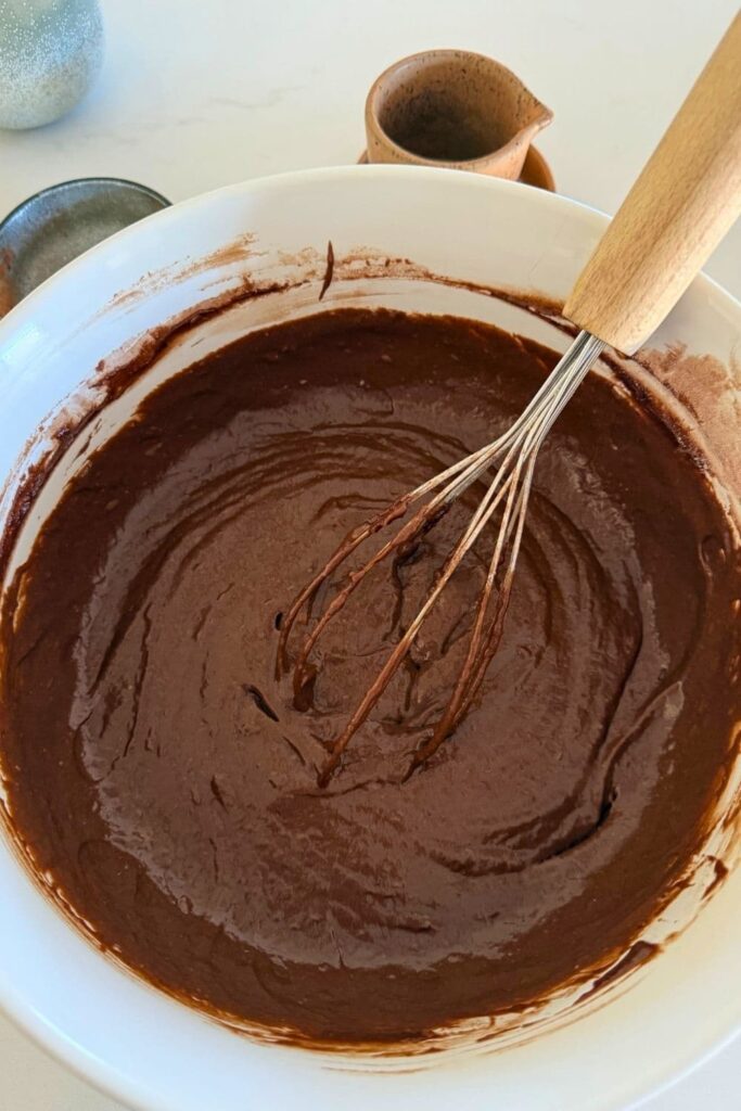 sourdough chocolate cupcake batter in white bowl with whisk.