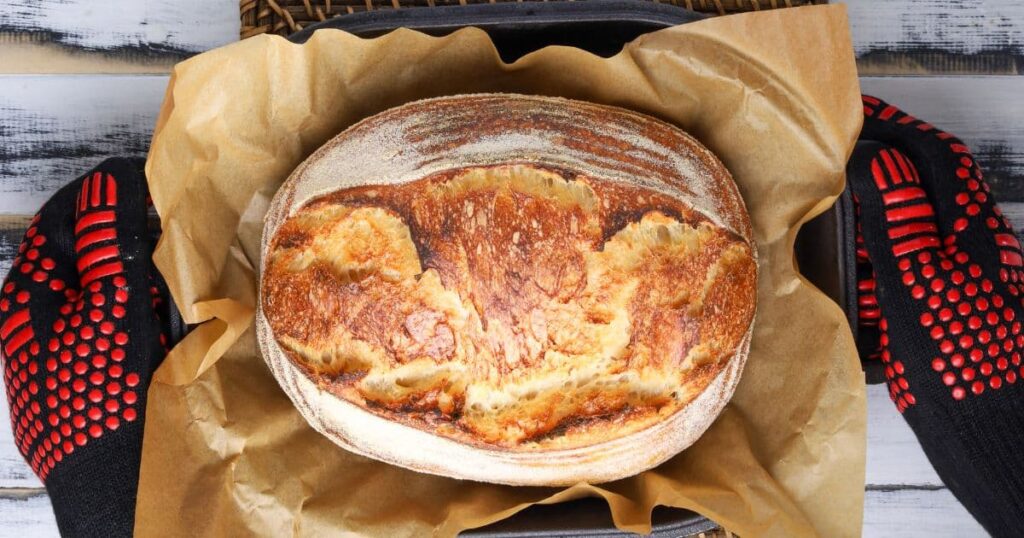 A photo showing a fresh sourdough loaf being taken out of the oven and set onto the counter.