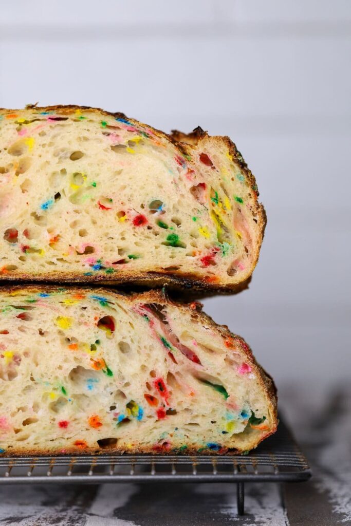 A loaf of sourdough funfetti bread cut in half and stacked on top of each other so that you can see the bright and colorful crumb inside.