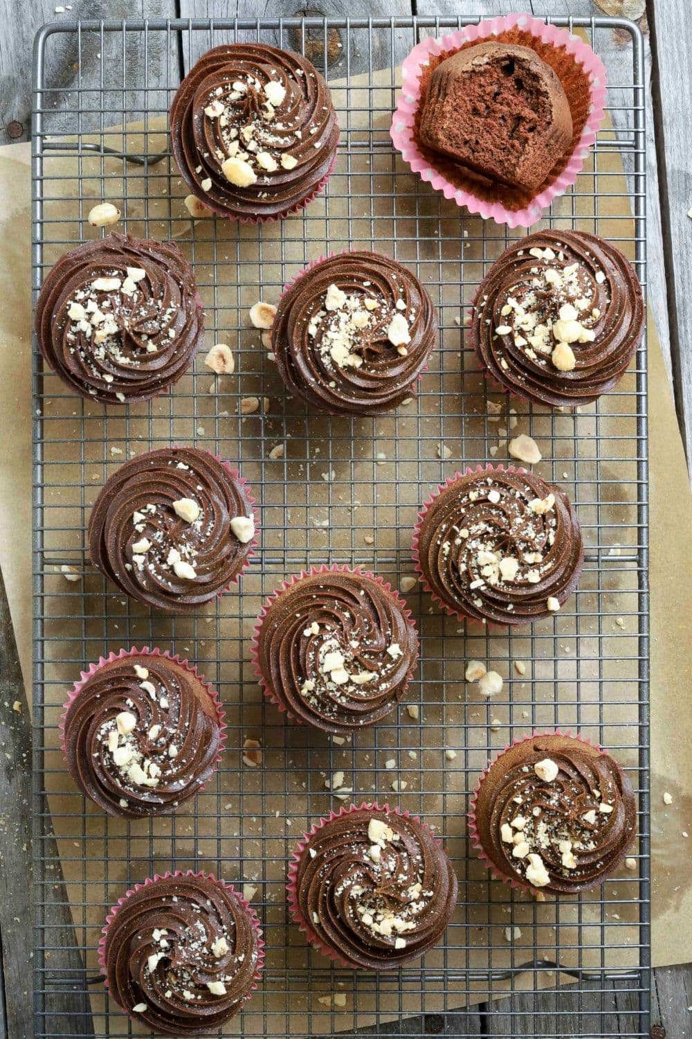 Sourdough chocolate cupcakes with buttercream frosting on a wire cooling rack with parchment paper underneath.