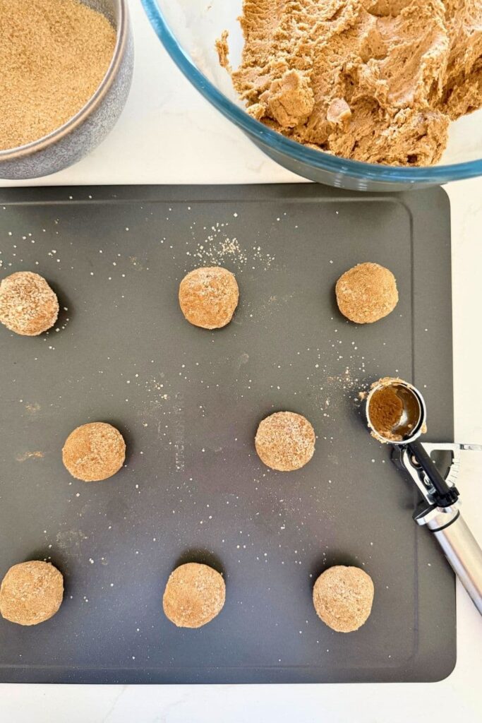sourdough ginger molasses cookie dough being scooped onto cookie sheet.
