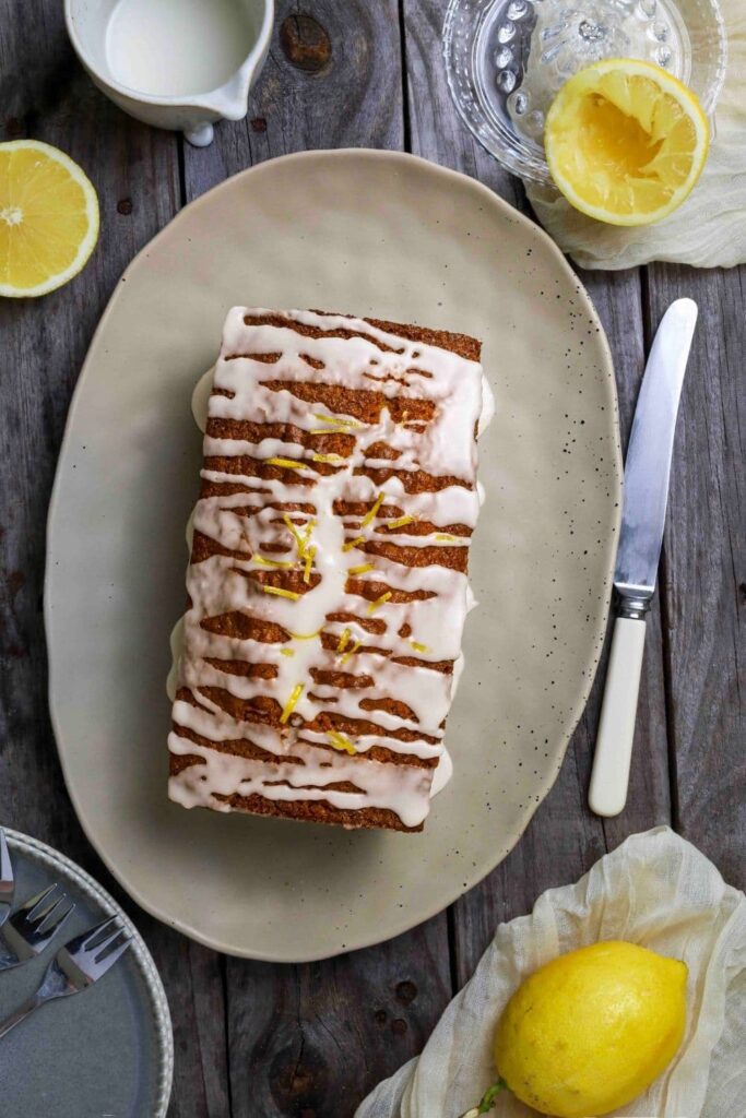 Sourdough Lemon loaf on serving plate next to a knife and lemons.