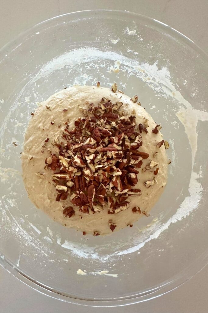 Adding chopped pecans to bread dough in a bowl to make sourdough maple pecan loaf.