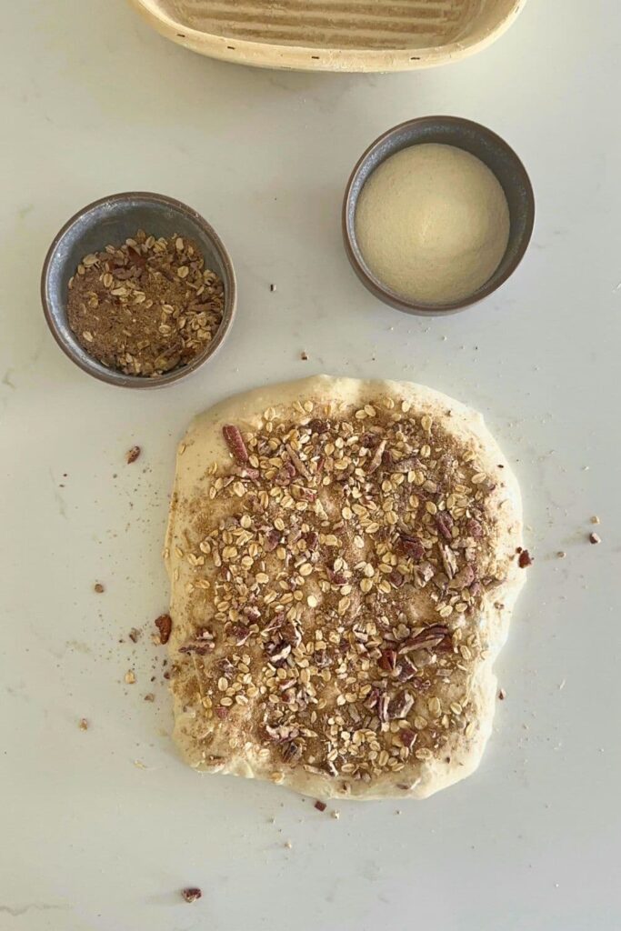 Shaping the sourdough maple pecan loaf with dough stretched on counter and adding spices.