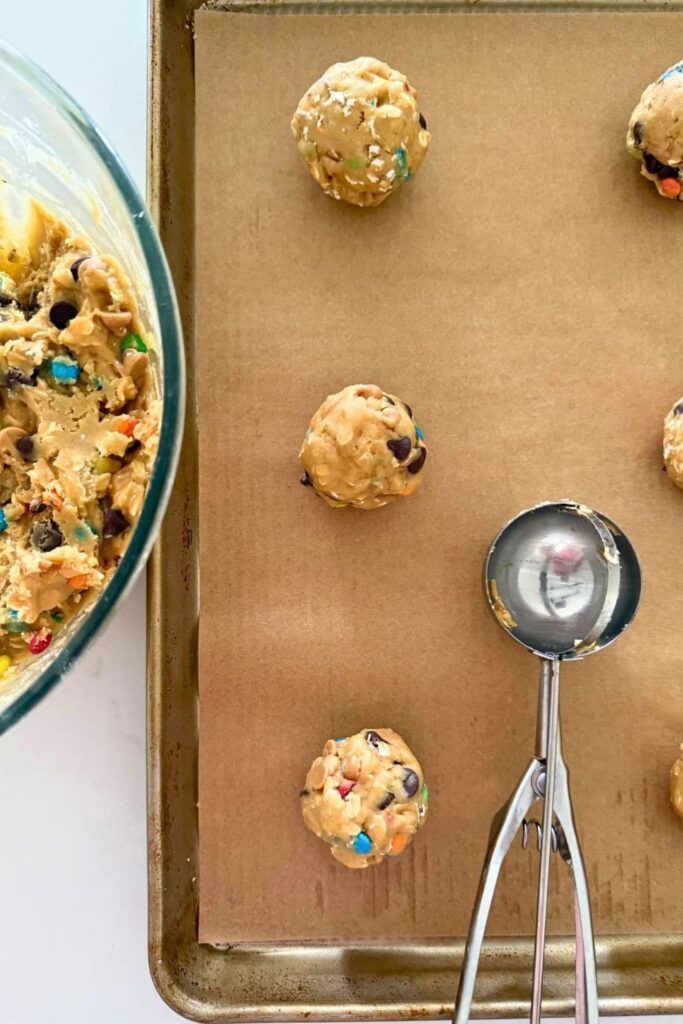 Sourdough monster cookie dough scooped with a cookie scooper onto baking sheet lined with parchment paper.