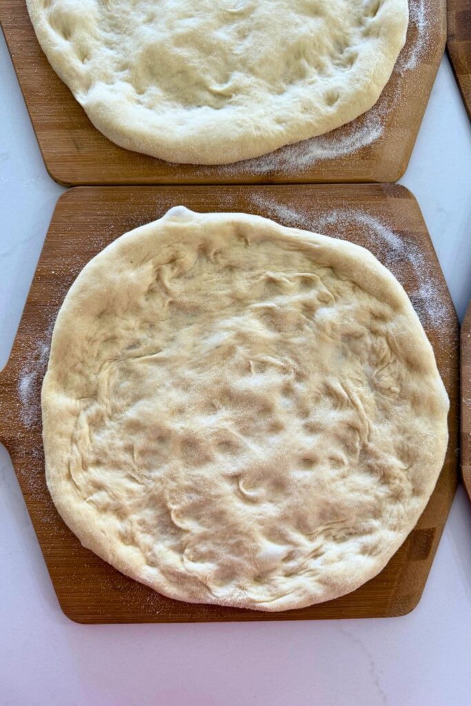 A sourdough pizza base sitting on a wooden pizza peel.