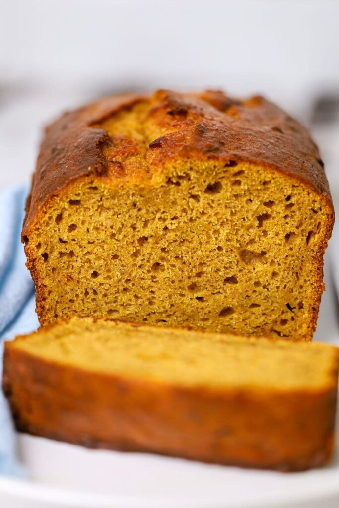 A close up image of a loaf of sourdough pumpkin banana bread that has been sliced open so you can see the tender, pumpkiny crumb inside.