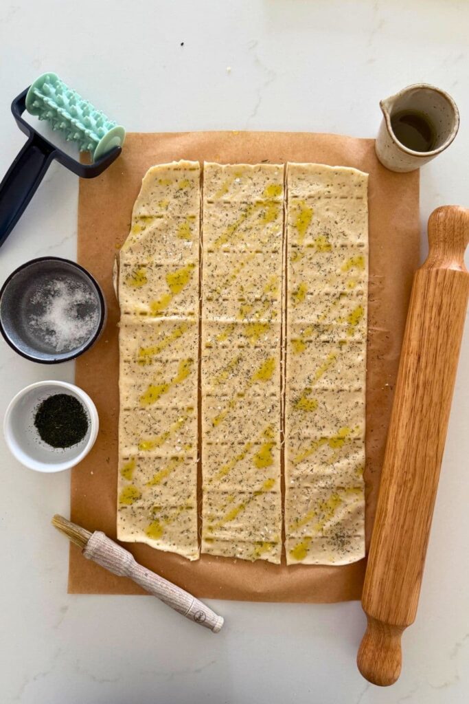 Sourdough ranch dough rolled out and cut with a cracker roller. There is also a rolling pin and small jug of oil in the photo.