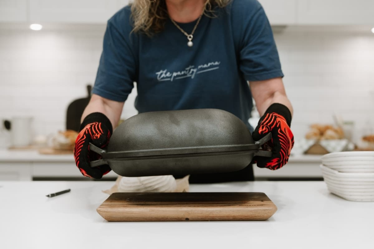 Kate Freebairn from The Pantry Mama holding a rectangle Cast Iron Bread Pan with red high heat oven gloves.