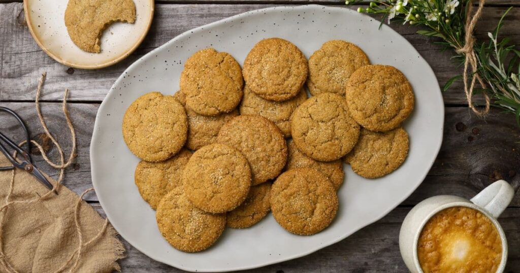 An oval platter filled with freshly baked sourdough ginger molasses cookies. There is also a cup of coffee in the photo.