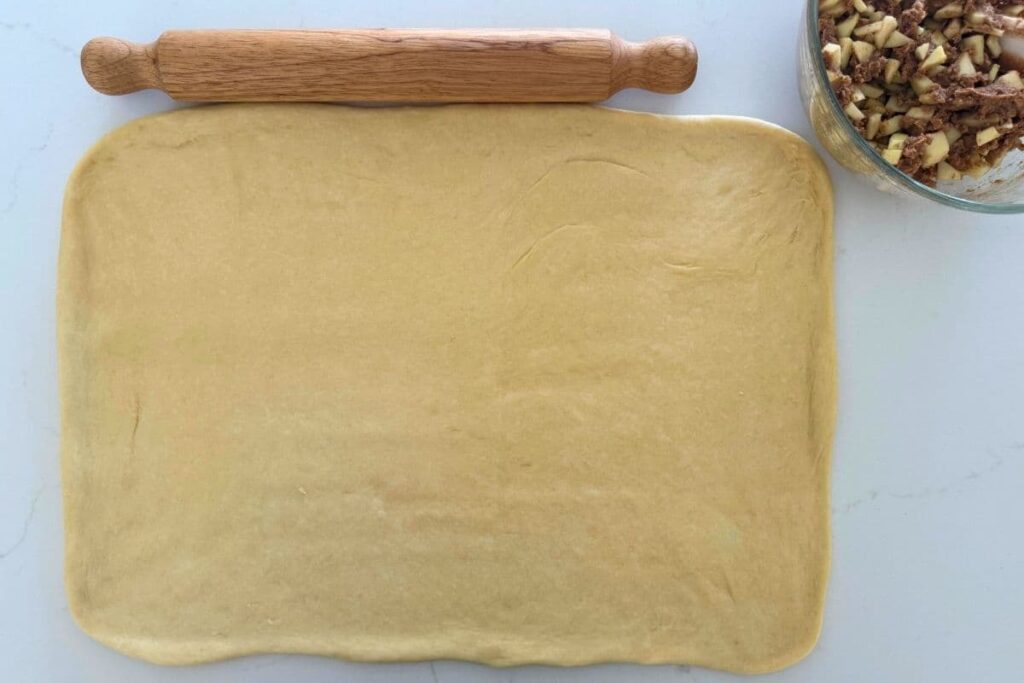 Sourdough apple cinnamon roll dough rolled out on counter next to rolling pin.