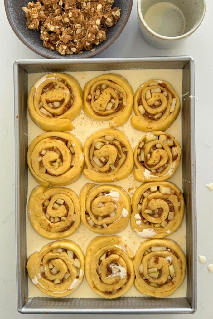 Sourdough apple cinnamon roll dough slices in baking dish with heavy cream poured in.