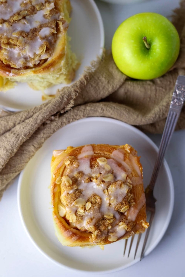 Sourdough apple cinnamon roll on a plate with an apple next to it.