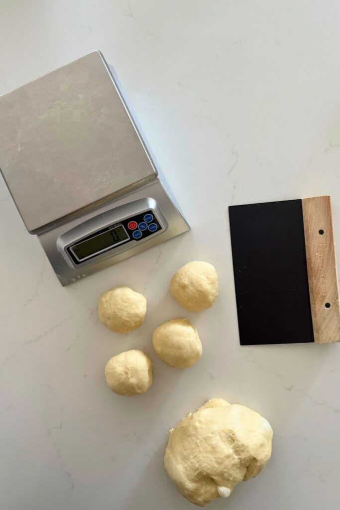 Sourdough burger bun dough with bench scraper and scale to portion out into bun dough balls.