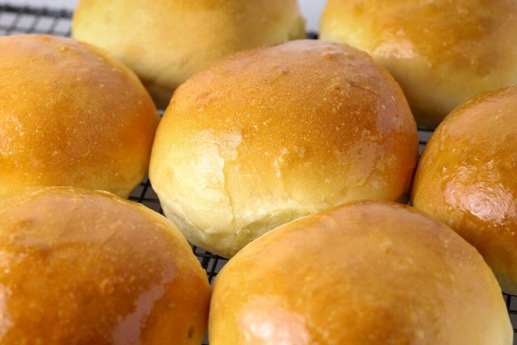 Sourdough burger buns on a wire rack. The buns have been brushed with butter so they are glossy and shining in the light.