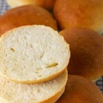 Sourdough burger buns on a wire rack with one sliced open.