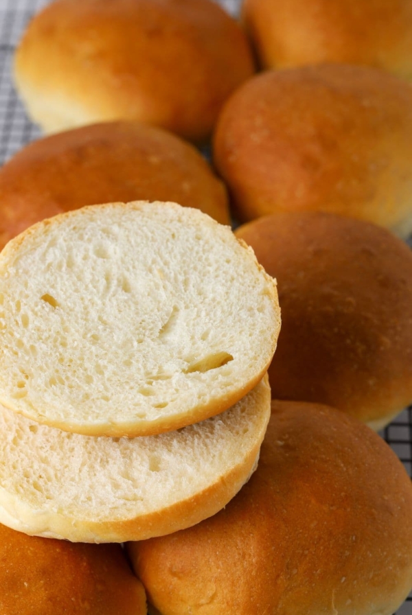 Sourdough burger buns on a wire rack with one sliced open.