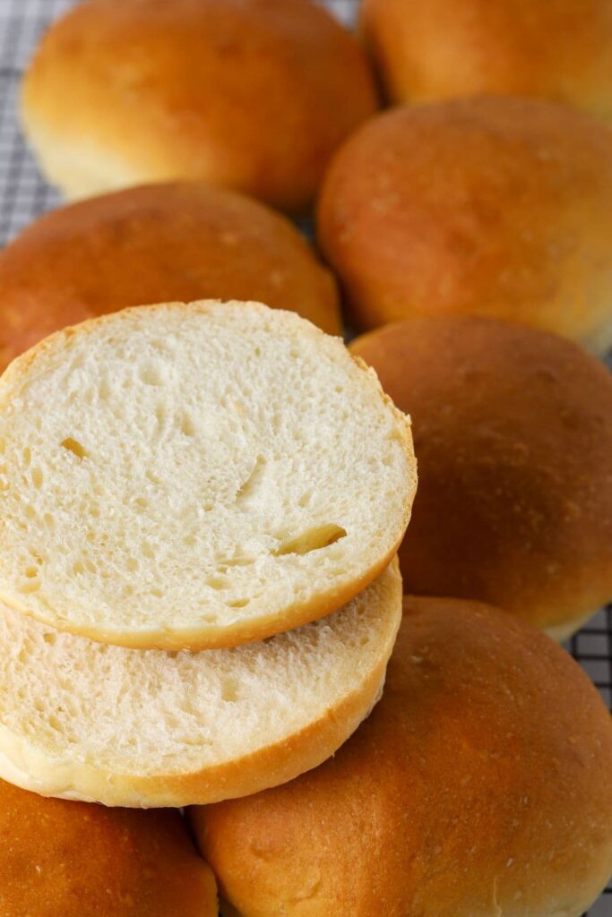 Sourdough burger buns on a wire rack with one sliced open.