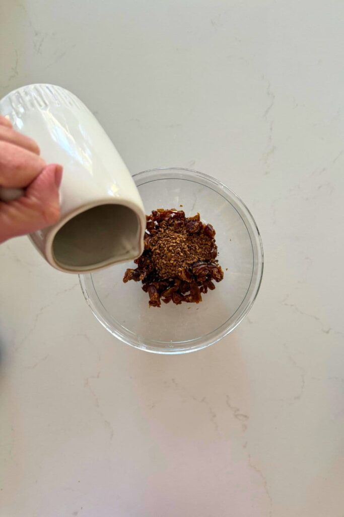 Pouring hot water on dates in a bowl to soak them to make sourdough date and walnut cookies.