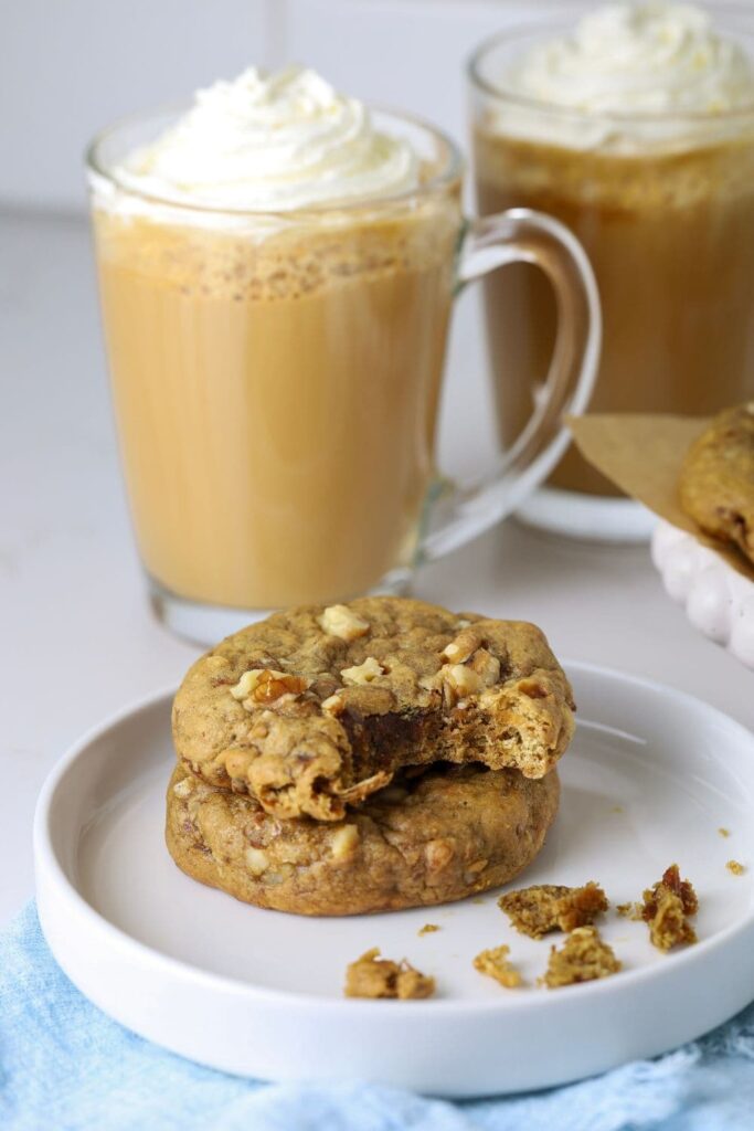 Two sourdough date and walnut cookies on a plate with hot coffees.