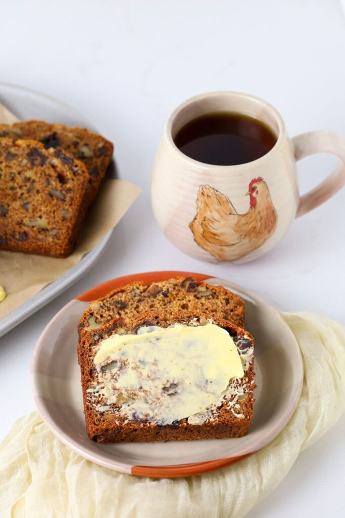 Sourdough date and walnut loaf cake slice on a plate with fresh butter.