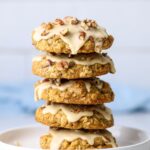 A stack of 5 maple pecan sourdough oatmeal cookies frosted with maple butter glaze sitting on a white plate. There is a pale blue napkin in the background.