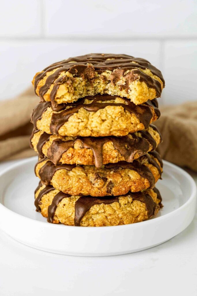 Sourdough Oatmeal Chocolate Chip Cookies stacked on a plate with a bite taken out of top cookie.