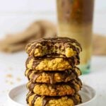 Sourdough Oatmeal Chocolate Chip Cookies stacked on a plate with a bite taken out of top cookie and an iced coffee in the background to drink with the cookies.