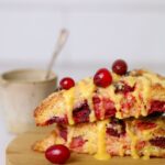 Sourdough orange cranberry scones stacked on wooden plate with fresh cranberries on top.