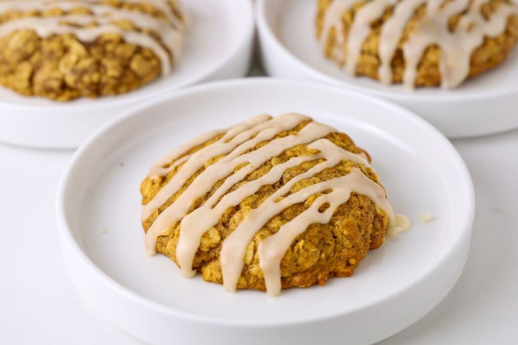 Sourdough pumpkin oatmeal cookie with glaze on top sitting on a small plate.
