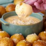 3 ingredient beer cheese dip served in a small green bowl. The bowl is surrounded by sourdough discard pretzel bites and one of the bites has been dipped into the beer cheese dip and is being suspended just above the bowl.