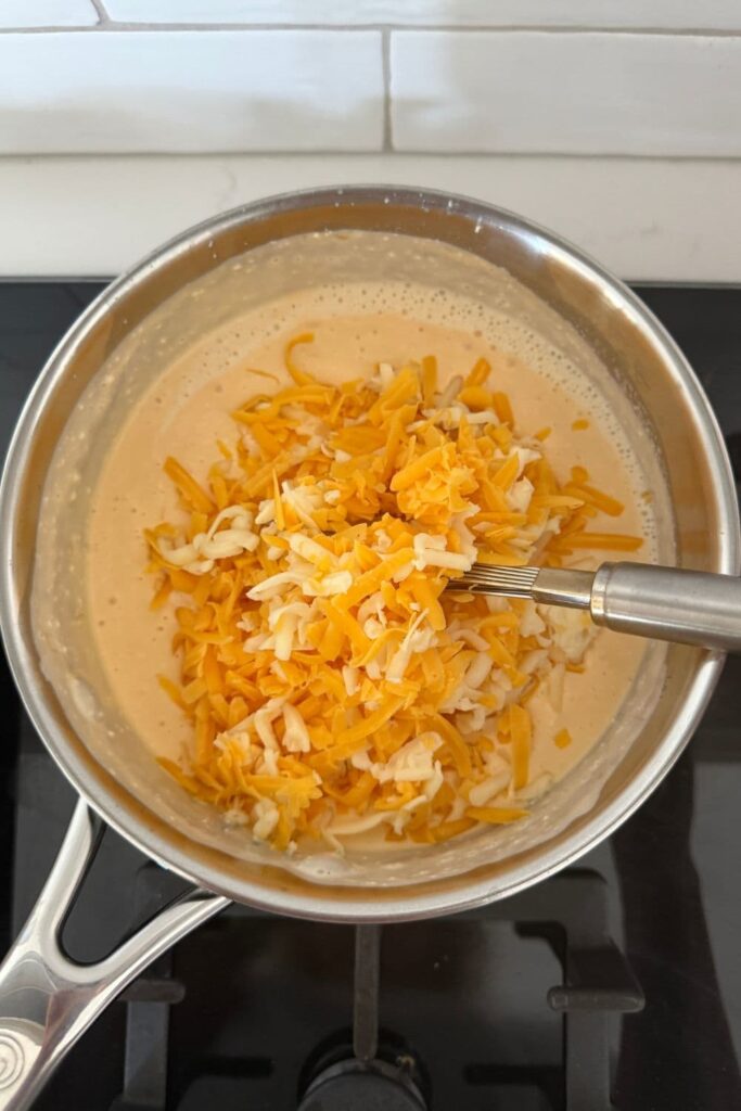 A saucepan of beer cheese dip where the cream cheese has been melted into the beer and the yellow cheddar cheese has just been added to the pot, it has not been whisked.