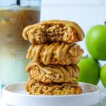 Four apple cinnamon sourdough oatmeal cookies stacked on a plate with a bite taken out of top cookie to show inside texture.