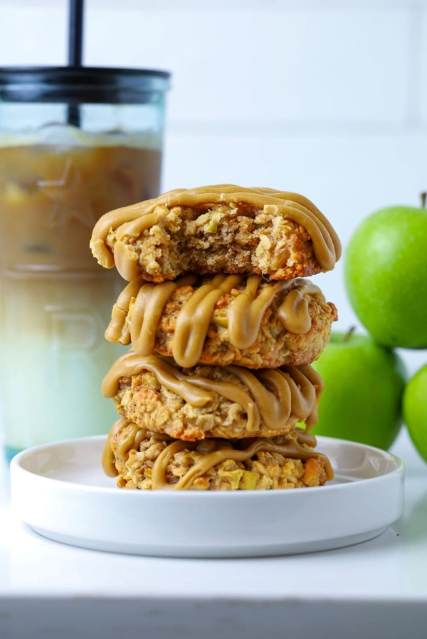 Four apple cinnamon sourdough oatmeal cookies stacked on a plate with a bite taken out of top cookie to show inside texture.