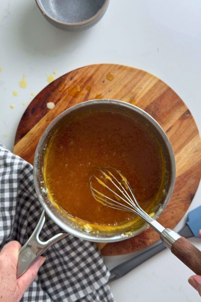 A saucepan of glossy homemade caramel sauce with a whisk inside.