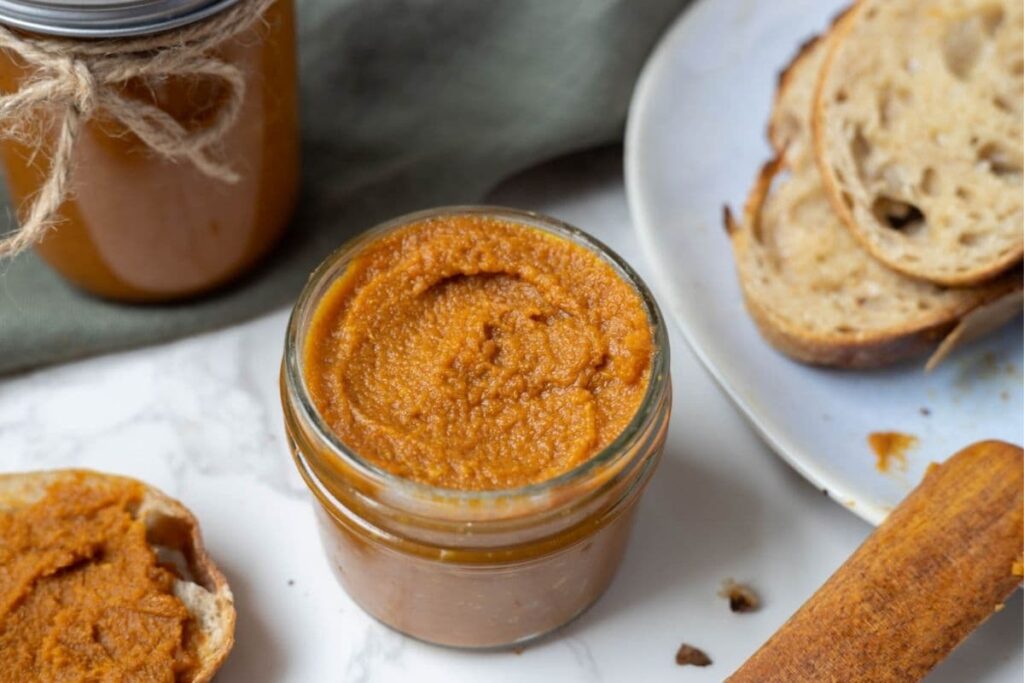 A full jar of pumpkin butter with no lid sitting on a white surface.