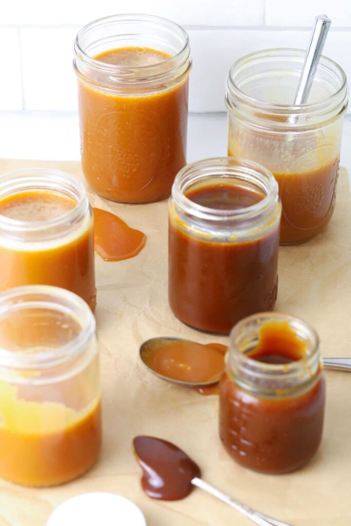 A selection of jars of caramel sauce that vary in colors from light to dark. The jars are sitting on a sheet of parchment paper.