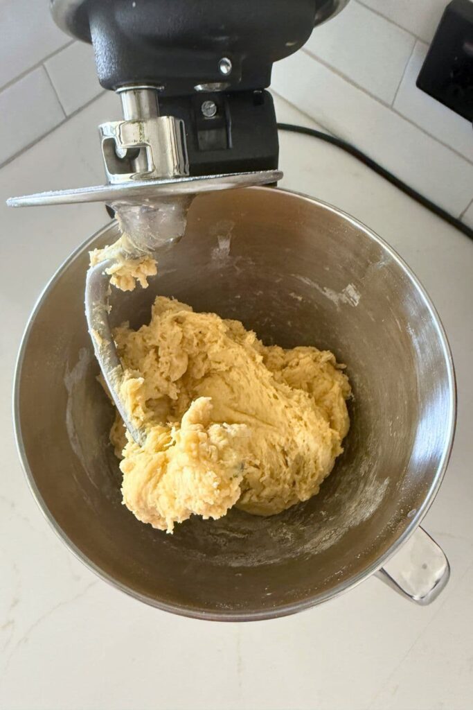 A stainless steel stand mixer bowl with a rough sourdough honey butter roll dough.