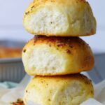 Three sourdough cheese and garlic rolls stacked on plate.