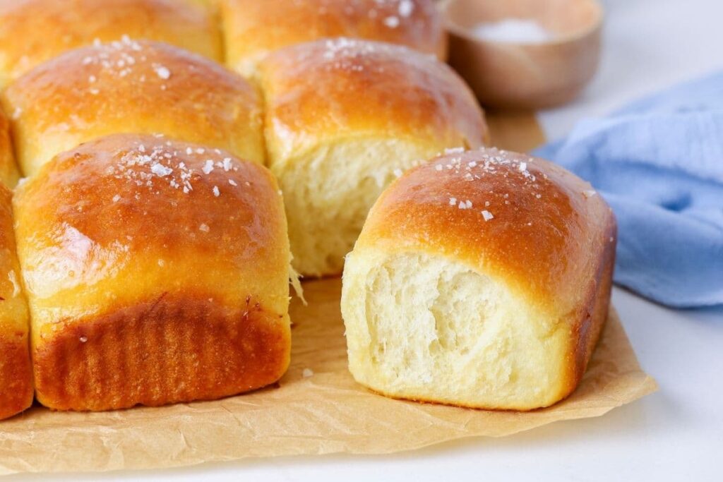 A horizontal image of sourdough discard honey dinner rolls. One of the rolls has been pulled away from the rest so you can see the fluffy inside.